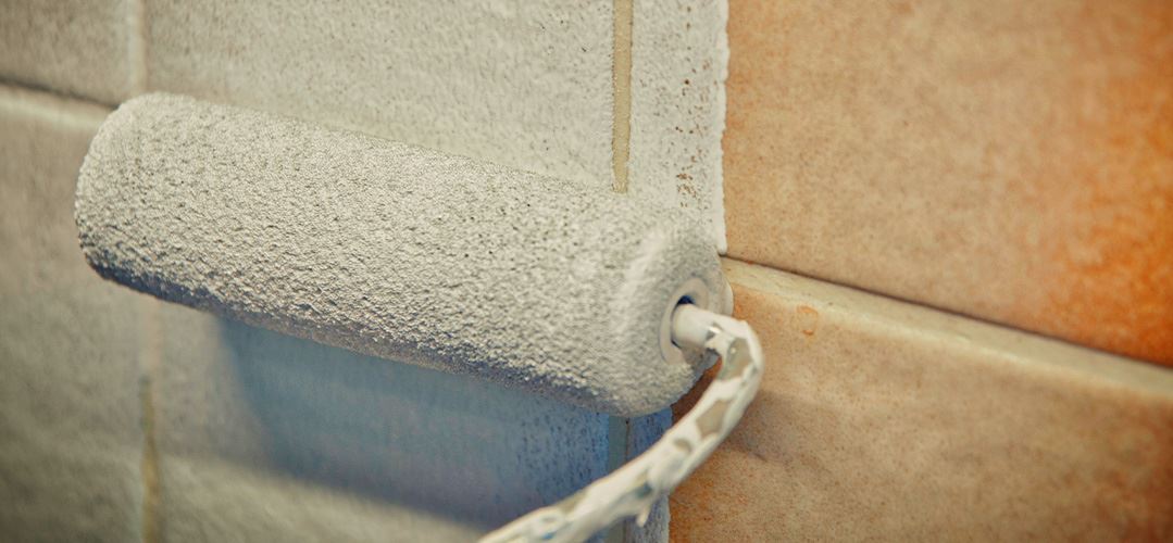 Paint roller rolling paint on a tile wall